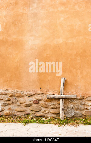 Ein handgemachtes rustikales Holzkreuz, das an einer Kirchenwand im Santuario de Chimayó, New Mexico, USA, ruht Stockfoto