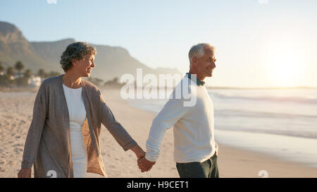 Im Freien Schuss älteres Paar zusammen am Strand spazieren. Senior Mann und ältere Frau bei einem Spaziergang am Ufer Meeres. Stockfoto