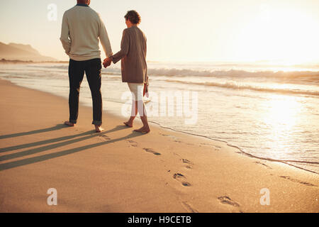 Rückansicht eines älteren Paares zu Fuß entlang der Küste. Reifer Mann und Frau zusammen ein Spaziergang am Meer bei Sonnenuntergang. Stockfoto