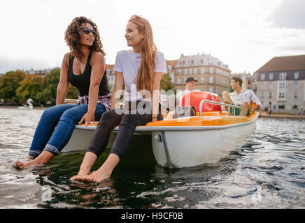 Aufnahme von zwei Frauen sitzen vor Tretboot mit Füßen im Wasser und der Mann im Hintergrund. Teenager Freunden genießen, Bootfahren im See. Stockfoto