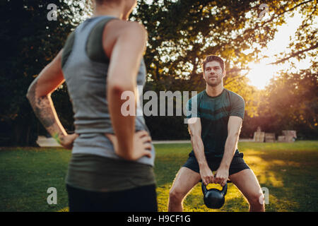 Junger Mann tun Krafttraining mit weiblichen Personaltrainer im Park. Kaukasische Männer mit Kettlebell Training. Stockfoto