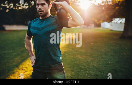 Schuss eines gesunden jungen Mannes, der mit Kettlebell arbeitet. Fitness männliches Modeltraining am Morgen im Park. Stockfoto