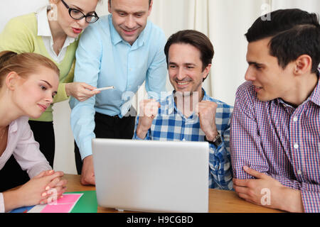 Gruppe von fröhlichen Geschäftsleute in lässig tragen Blick auf den Laptop zusammen und Lächeln auf den Lippen Stockfoto