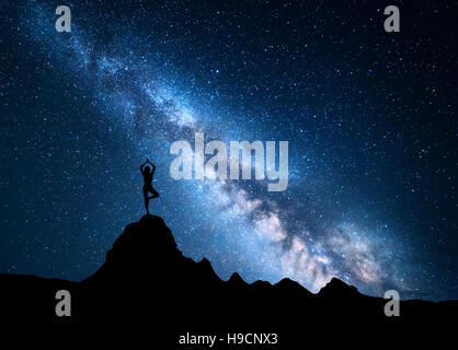 Milky Way mit Silhouette einer stehenden Frau praktizieren Yoga auf Berg. Landschaft mit Meditierenden Mädchen Stockfoto