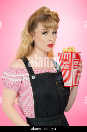 Pin-up Girl mit Karton auf Popcorn auf einem hellen rosa Hintergrund Stockfoto