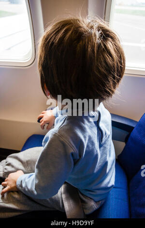 Kaukasier Kind, Junge, 4-6 Jahre alt, im Flugzeug Sitz sitzt schaut aus dem Fenster. Gesicht wurde entfernt. Stockfoto