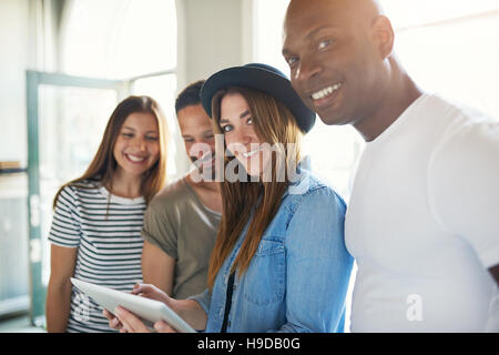 Junge trendige lächelnd Gruppe von vier Freunden mit Tablet Spaß und Blick in die Kamera im Sonnenlicht. Stockfoto