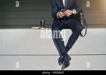 Gekreuzten Beinen der Geschäftsmann mit Handy sitzen. Horizontal im Freien gedreht Stockfoto