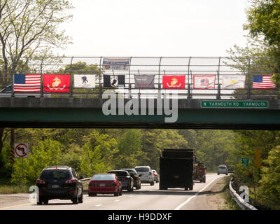 Eine US-Flagge sowie Flaggen der US militärischen Services werden auf einer Brücke über einem Massachusetts Highway unter Beachtung des Memorial Day angezeigt. Beachten Sie Prisoner Of War (POW) Flagge in Mitte. Stockfoto