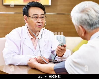 asiatischen Arzt Blutdruckmessung eines älteren Patienten mit Blutdruckmessgerät Stockfoto