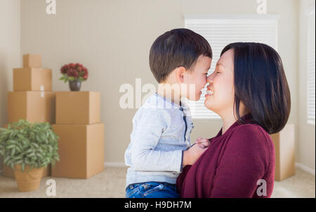 Young gemischt Rennen Chinesisch Mutter und Kind im leeren Raum mit gepackten Umzugskartons und Pflanzen. Stockfoto