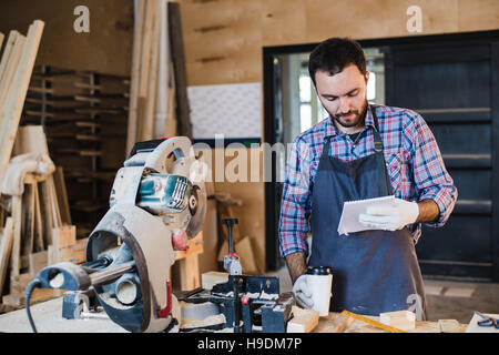 Zimmermann, eine Kaffee-Pause halten Notebook vor Kreissäge in seiner Werkstatt Stockfoto