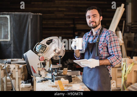 Zimmermann, eine Kaffee-Pause halten Notebook vor Kreissäge in seiner Werkstatt Stockfoto