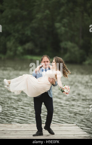 Bräutigam trägt Braut in der Nähe von See und Wald Stockfoto