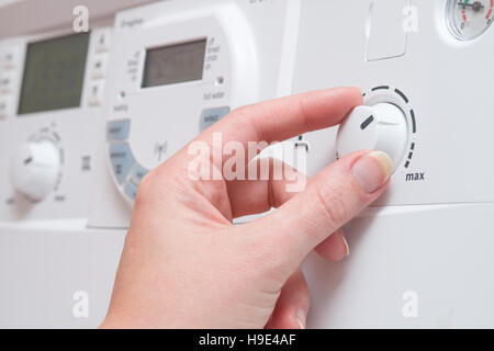 Eine Hand passen Sie das Zifferblatt controlling Wassertemperatur auf einem weißen Kessel. Es scheint, drehen in Richtung zu den MAX-Einstellung.  Andere Tasten und ein digitales Stockfoto