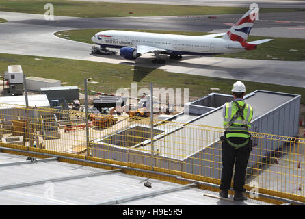 Ein Arbeitnehmer stellt ein Gerüst auf dem Dach des neuen Terminal 2 am Flughafen London Heathrow. Flugzeuge-Taxi im Hintergrund. Stockfoto