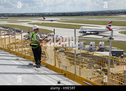 Ein Arbeitnehmer stellt ein Gerüst auf dem Dach des neuen Terminal 2 am Flughafen London Heathrow. Flugzeuge-Taxi im Hintergrund. Stockfoto
