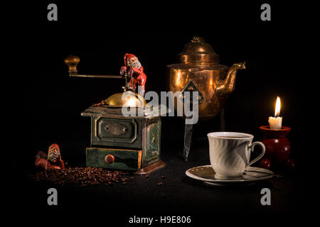 Kaffee-Weihnachtszeit, Stillleben mit Tomtes auf eine alte Kaffeemühle, Kaffee-Wasserkocher und eine Kaffeetasse auf einem schwarzen Hintergrund. Stockfoto