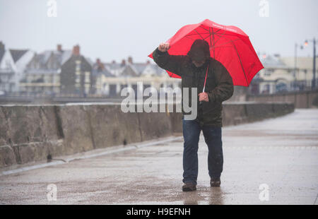 Ein Mann Schlachten starken Winden mit einem roten Regenschirm bei Sturm Angus in Porthcawl, South Wales, UK. Stockfoto