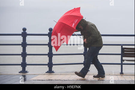 Ein Mann Schlachten starken Winden mit einem roten Regenschirm bei Sturm Angus in Porthcawl, South Wales, UK. Stockfoto