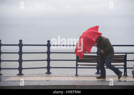 Ein Mann Schlachten starken Winden mit einem roten Regenschirm bei Sturm Angus in Porthcawl, South Wales, UK. Stockfoto