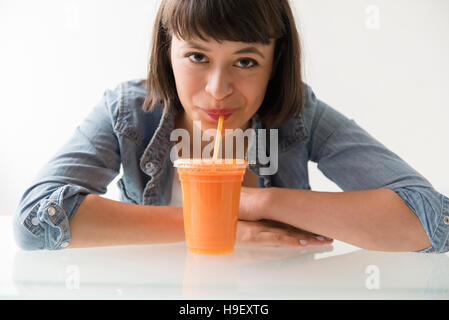 Hispanic Frau trinken orange Smoothie mit Stroh Stockfoto