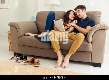 Junges Paar auf dem Sofa sitzen und beobachten etwas auf einem tablet Stockfoto