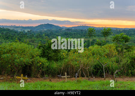 Einfache hölzerne Kreuze und Gräber vor üppigen Dschungel und dramatischen Sonnenuntergang im Kongo Stockfoto