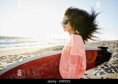 Hispanic Frau mit Surfbrett am Strand Stockfoto
