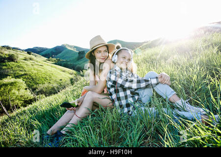 Mutter und Tochter sitzen auf Hügel Kopfhörer anhören Stockfoto