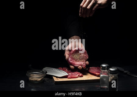 Nahaufnahme von mans Hände würzen das Fleisch Stockfoto