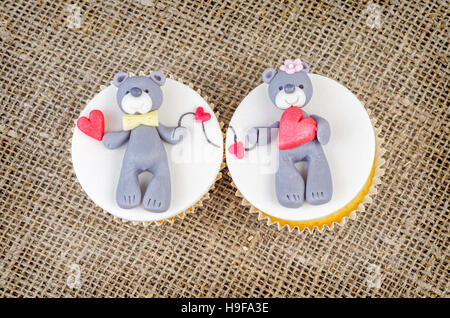 Cupcakes mit Teddy Bären und Herzen auf rustikale Jute Hintergrund. Valentinstag Kuchen. Stockfoto