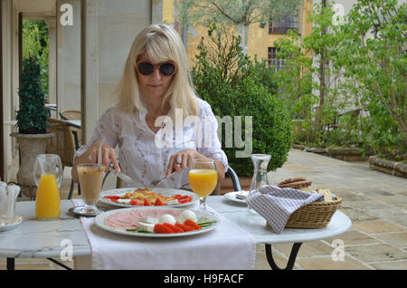 Blonde Frau, die amerikanisches Frühstück am Tisch serviert für zwei Personen Stockfoto