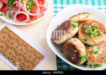 Draufsicht auf hausgemachte gebratene Fleischbällchen in einer Schüssel weiß, Salat von rohem Gemüse und Vollkorn Zwieback auf einer grünen Tischdecke Stockfoto