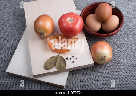 Zutaten zum Kochen im Vintage-Stil - Ei, Zwiebel, Tomaten, Knoblauch und Gewürze, hölzernen Planken und eine Tasse auf Textil-Hintergrund Stockfoto