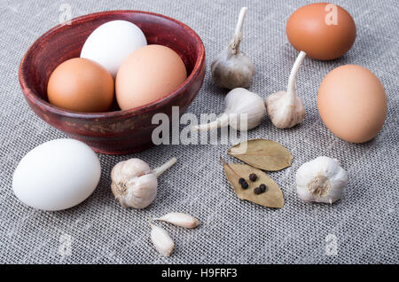 Detailansicht auf Hühnereier, Knoblauch und Gewürze auf dem Küchentisch auf dem alten grauen Textil-Hintergrund Stockfoto