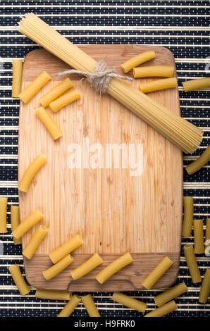 Essen-Hintergrund mit Zutaten auf den Tisch, Holzsockel, ein paar dünne Spaghetti und Nudeln auf einem gestreiften Hintergrund Stockfoto