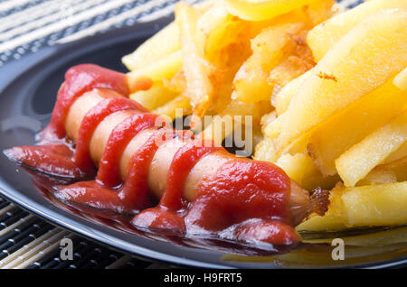 Detail einer schwarzen Platte mit gegrillten Würstchen mit Tomaten-Sauce und Bratkartoffeln closeup Stockfoto