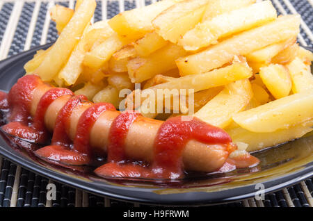 Gebratene Wurst und Pommes frites dekoriert mit Tomatensauce mit einer dunklen Platte Großaufnahme Stockfoto