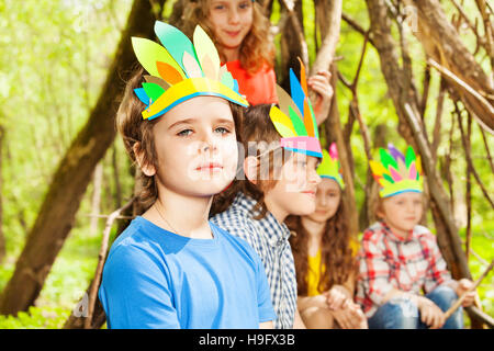 Süsser Boy in Injuns Kopfschmuck mit Freunden zu spielen Stockfoto