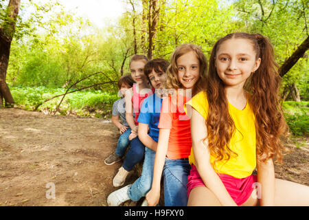 Niedliche glückliche Kinder sitzen auf einem Baumstamm im Wald Stockfoto