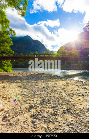 Japanische Touristen zu Fuß über Kappa-Bashi Brücke überspannt alpine Gewässer von Azusa River mit dramatischen Morgen Sonnenstrahlen in Kamikochi Stockfoto