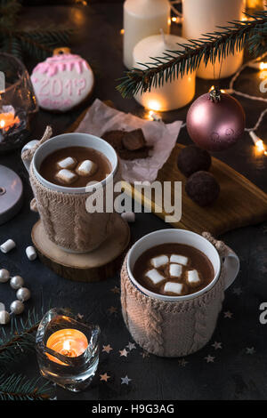 Zwei Tassen in gestrickte Handschuhe frischen heißen Kakao oder Schokolade auf hölzernen Weihnachten Hintergrund, dunkles Foto Stockfoto