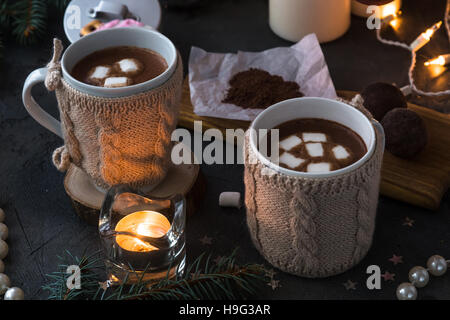 Zwei Tassen in gestrickte Handschuhe frischen heißen Kakao oder Schokolade auf hölzernen Weihnachten Hintergrund, dunkles Foto Stockfoto