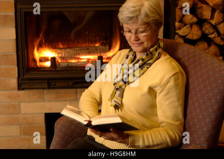 Frau liest ein Buch am Kamin Stockfoto