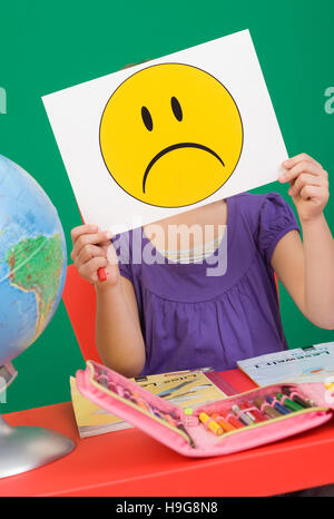 Mädchen an ihrem Schreibtisch, trauriger Smiley, symbolisches Bild für Probleme in der Schule Stockfoto