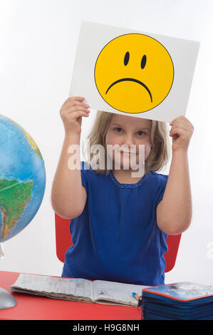 Mädchen an ihrem Schreibtisch, trauriger Smiley, symbolisches Bild für Probleme in der Schule Stockfoto