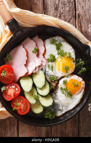 Spiegeleier mit Schinken und frischem Gemüse Nahaufnahme in einer Pfanne auf dem Tisch. vertikale Ansicht von oben Stockfoto