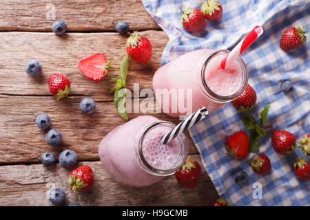 Milchshakes mit Erdbeeren und Heidelbeeren in Nahaufnahme der Flaschen auf den Tisch. horizontale Ansicht von oben Stockfoto