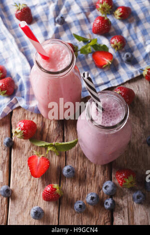Milchshakes mit Erdbeeren und Heidelbeeren in Nahaufnahme der Flaschen auf den Tisch. Vertikale Ansicht von oben Stockfoto